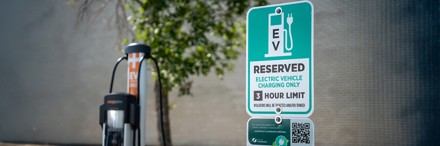 A parking sign reading "reserved for electric vehicles" in the foreground and an electric venicle charging station in the background